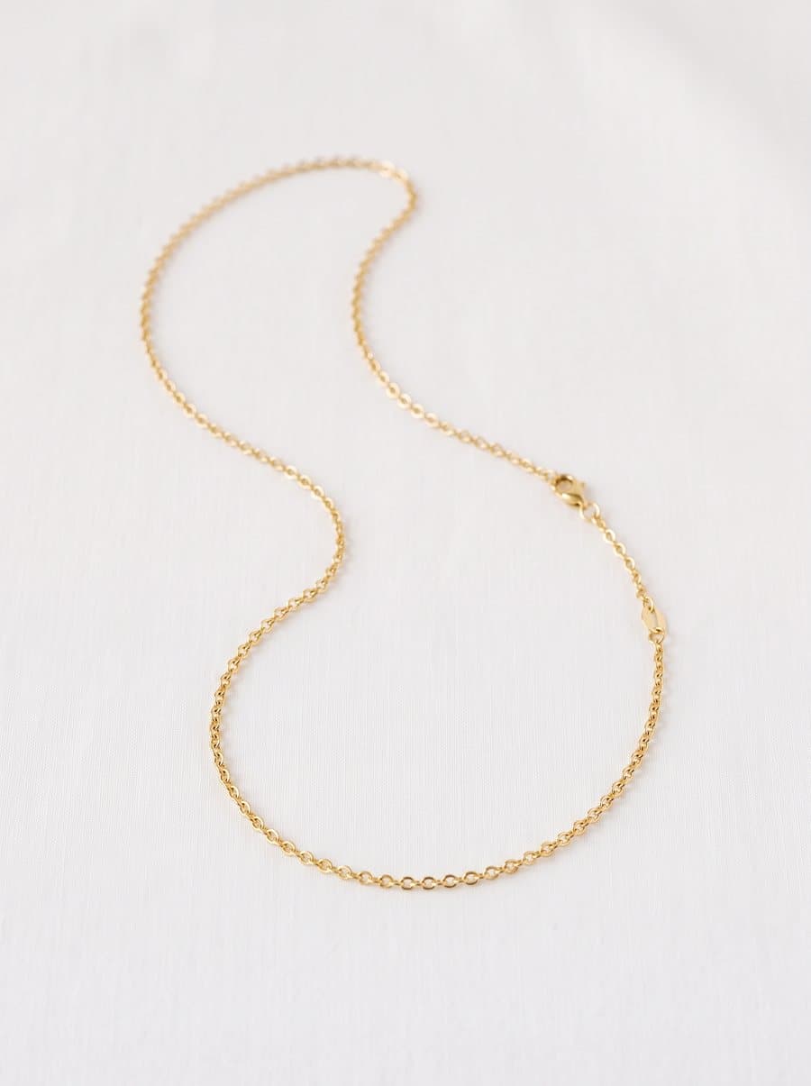Gold chain necklace laid in a curve on white